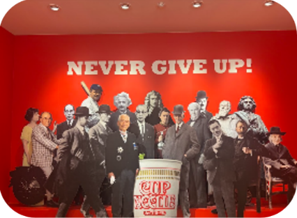 赤い壁に「NEVER GIVE UP!」の文字と、偉人たちに囲まれたカップヌードルの展示